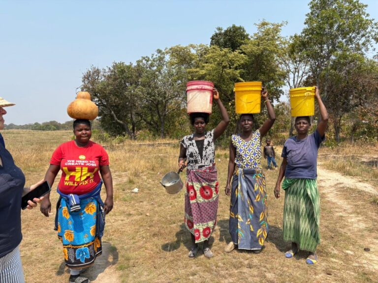 Menschen gehen mit Eimern auf ihren Köpfen zum Wasserloch.